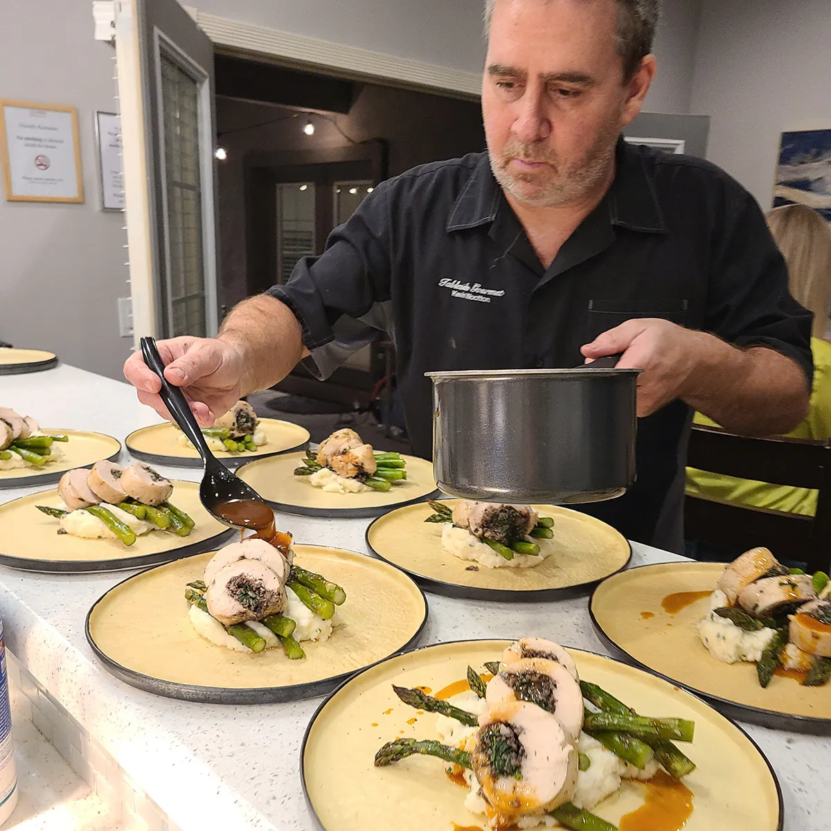 The chef is preparing a dish with pork, asparagus and mashed potatoes.