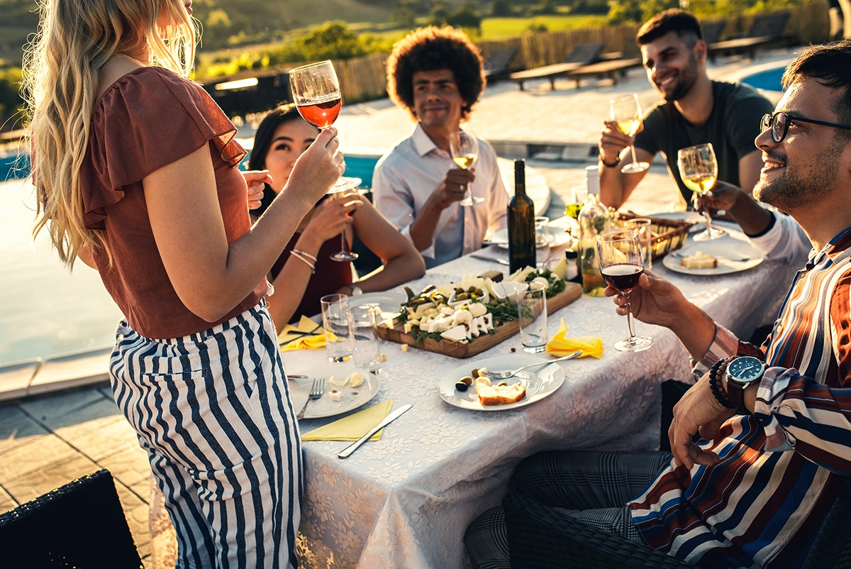 Poolside outdoor dinner party in Scottsdale, Arizona with guests enjoying wine, elegant luxury catering, cheese platters, and festive Fourth of July dining in a sunlit setting.