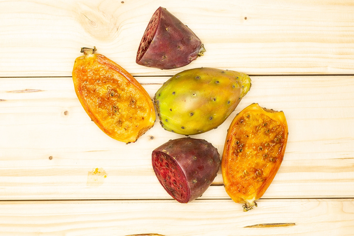 A vibrant flat-lay of fresh prickly pear cactus fruit, freshly cut to reveal its orange, red, and green hues, arranged on a rustic wooden surface that accentuates the fruit's bright colors and intriguing textures.