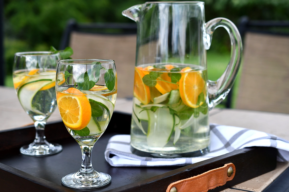 Elegant infused water and zero-proof cocktails with cucumber, orange, and fresh mint served in glassware at a summer dinner party.