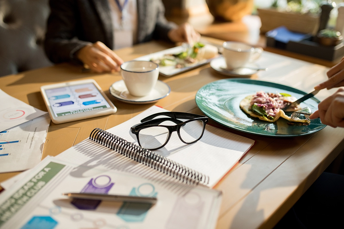 Business professionals enjoying plated lunches beside meeting documents, notepads, and a tablet during a working board meeting in Scottsdale.