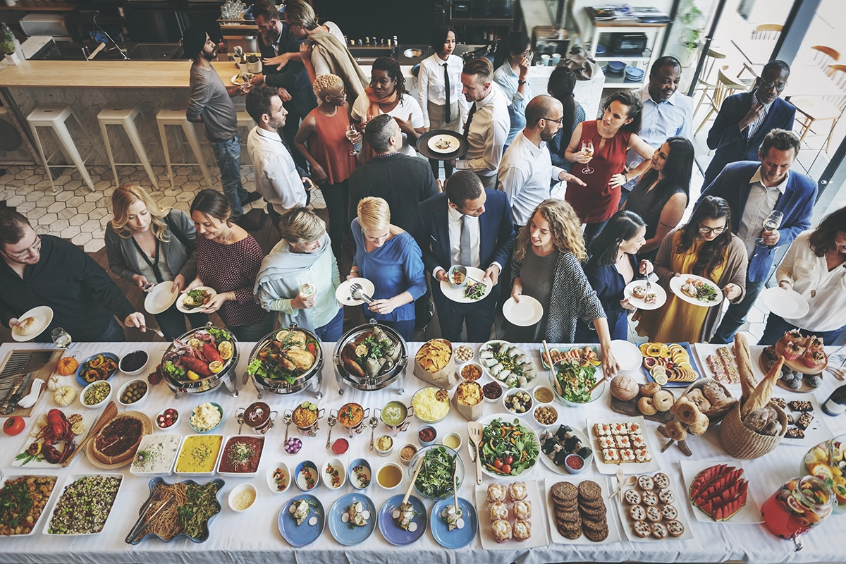 Corporate team members enjoying a catered buffet lunch in a Scottsdale office breakroom, serving themselves from a selection of labeled salads, entrées, and desserts.