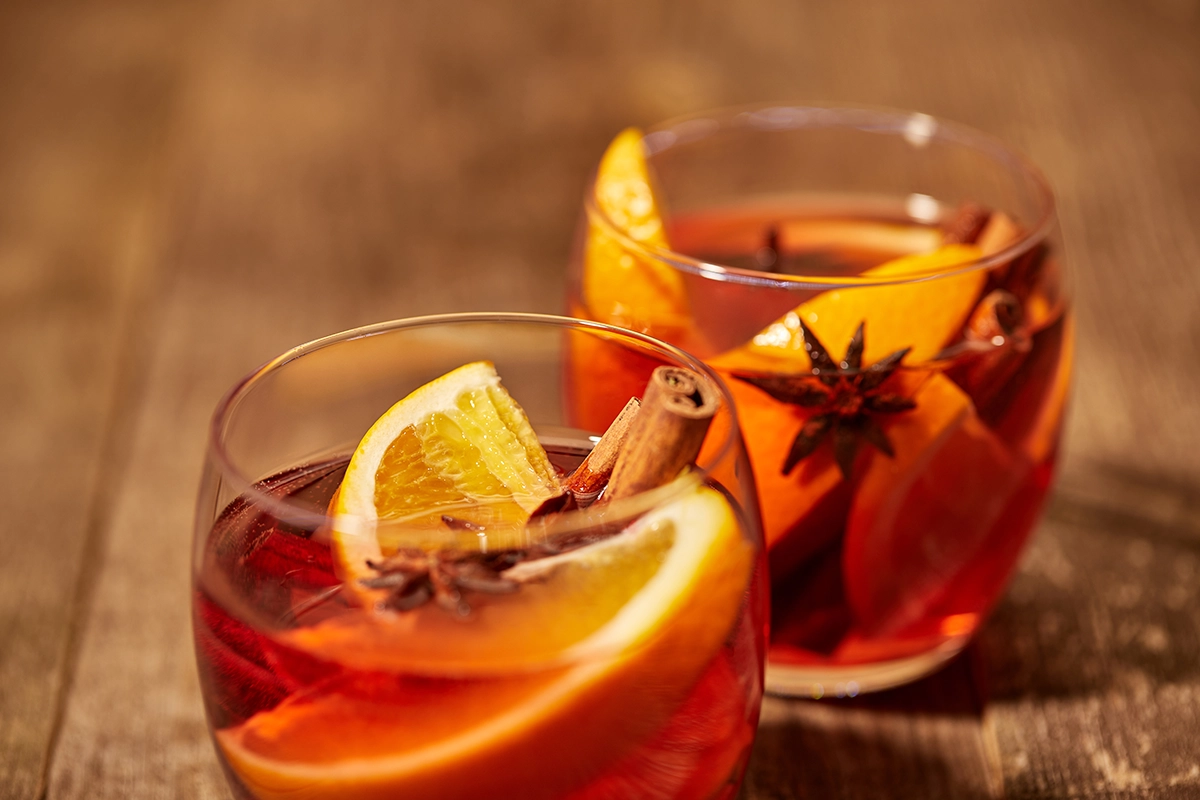 Two matching glasses of mulled wine garnished with orange slices, cinnamon sticks, and star anise on a wooden surface.