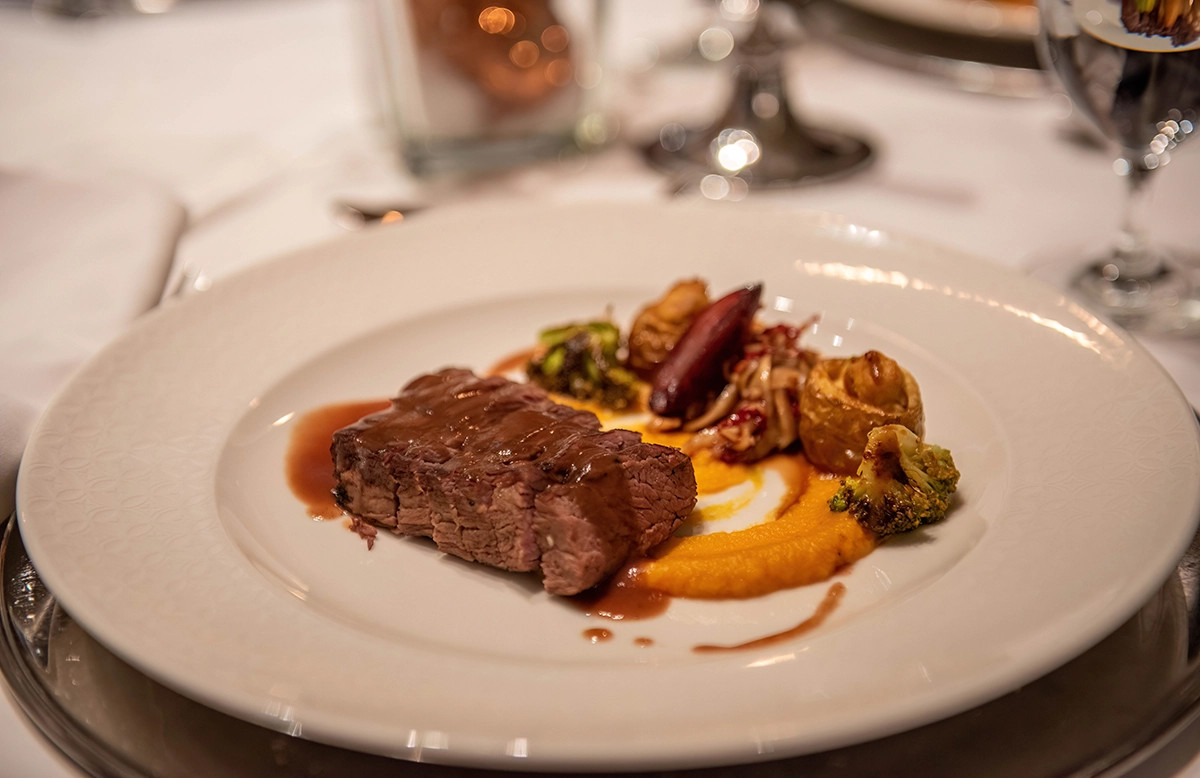 Steak with rich brown sauce, vegetables, and a bright orange purée, plated for an elegant wedding dinner.