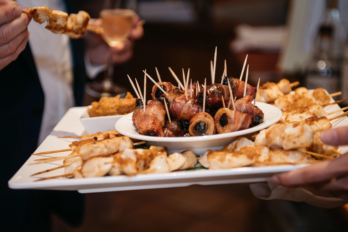 A server offering a tray of one-bite hors d’oeuvres, such as bacon-wrapped dates
