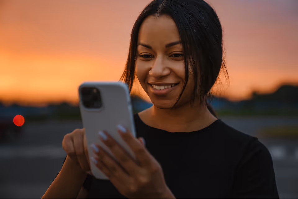 Smiling woman using a smartphone with a sunset background.