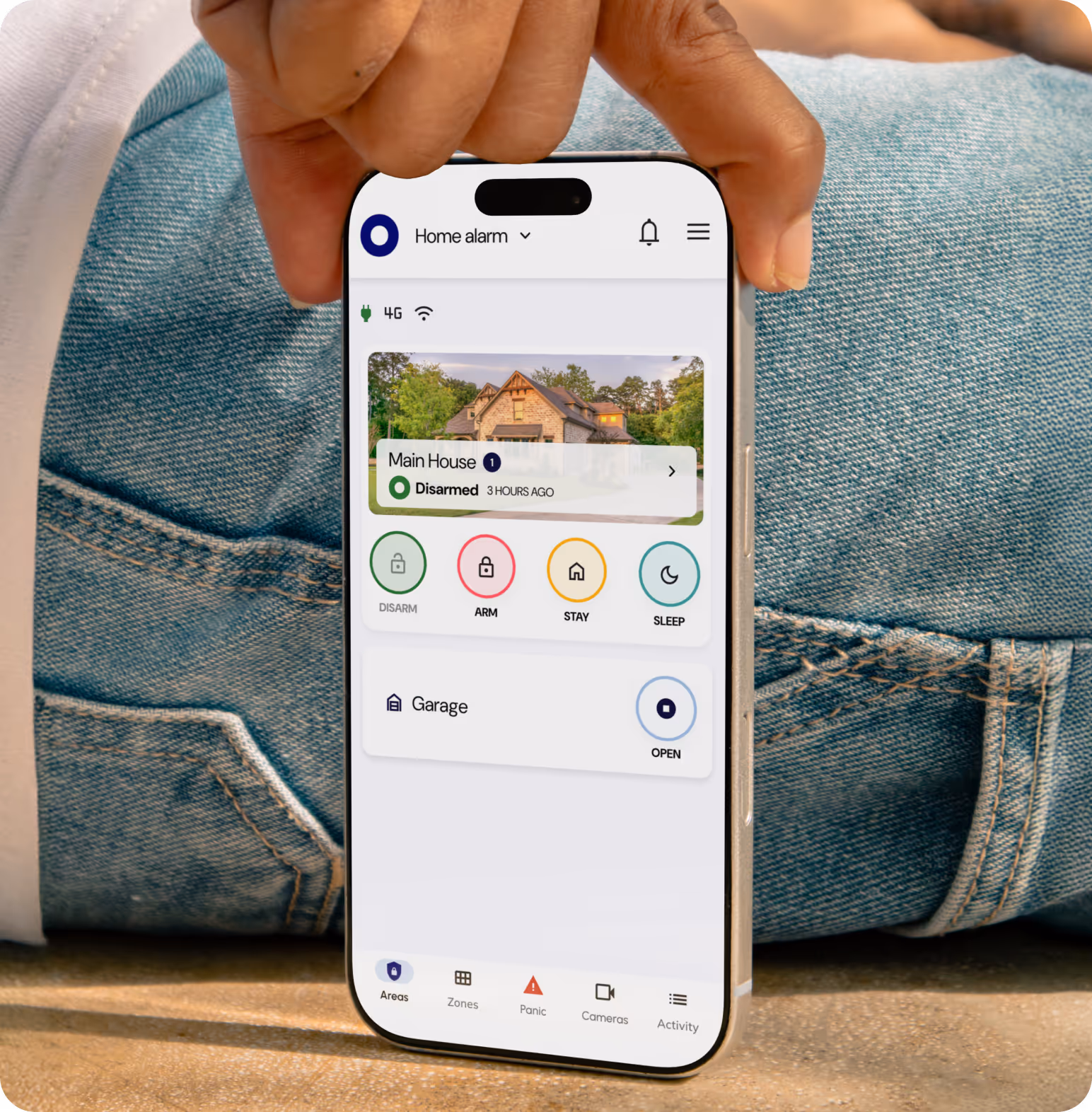 Hand holding smartphone with a home security app showing main house disarmed and garage door open controls.