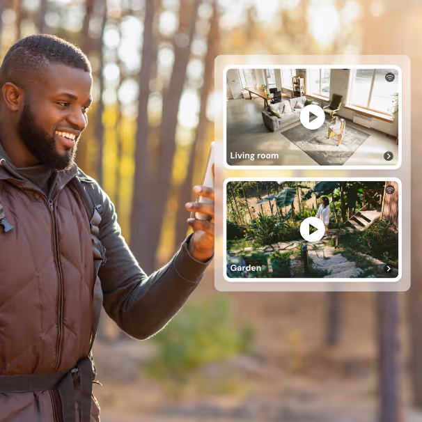Man outdoors smiling and holding phone with app screens showing living room and garden video feeds.