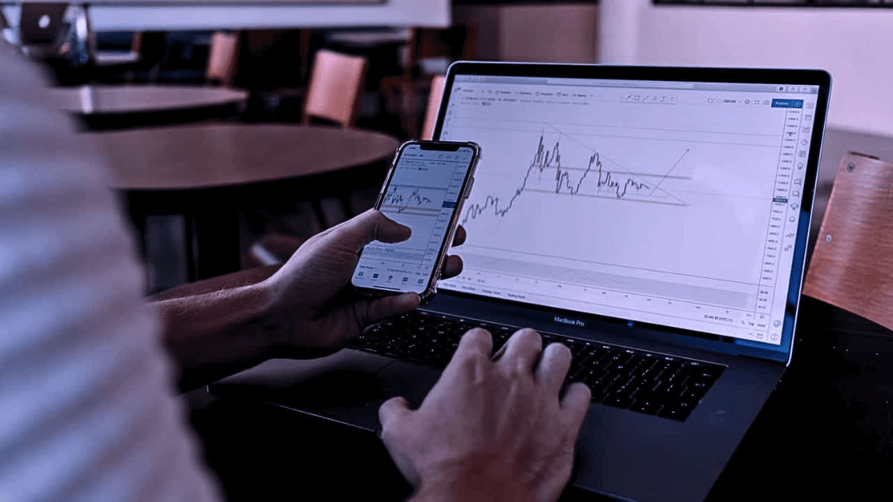 Person working on trade charts on multiple devices -  Is Day Trading Profitable