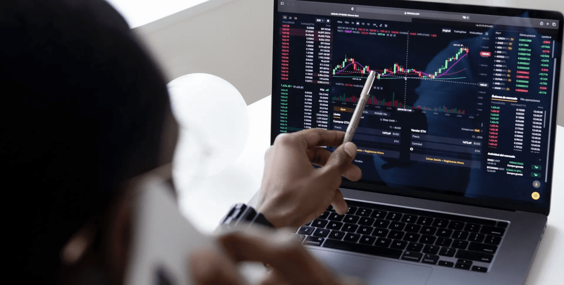 Man pointing pen at laptop - How to Learn Stock Trading for Beginners