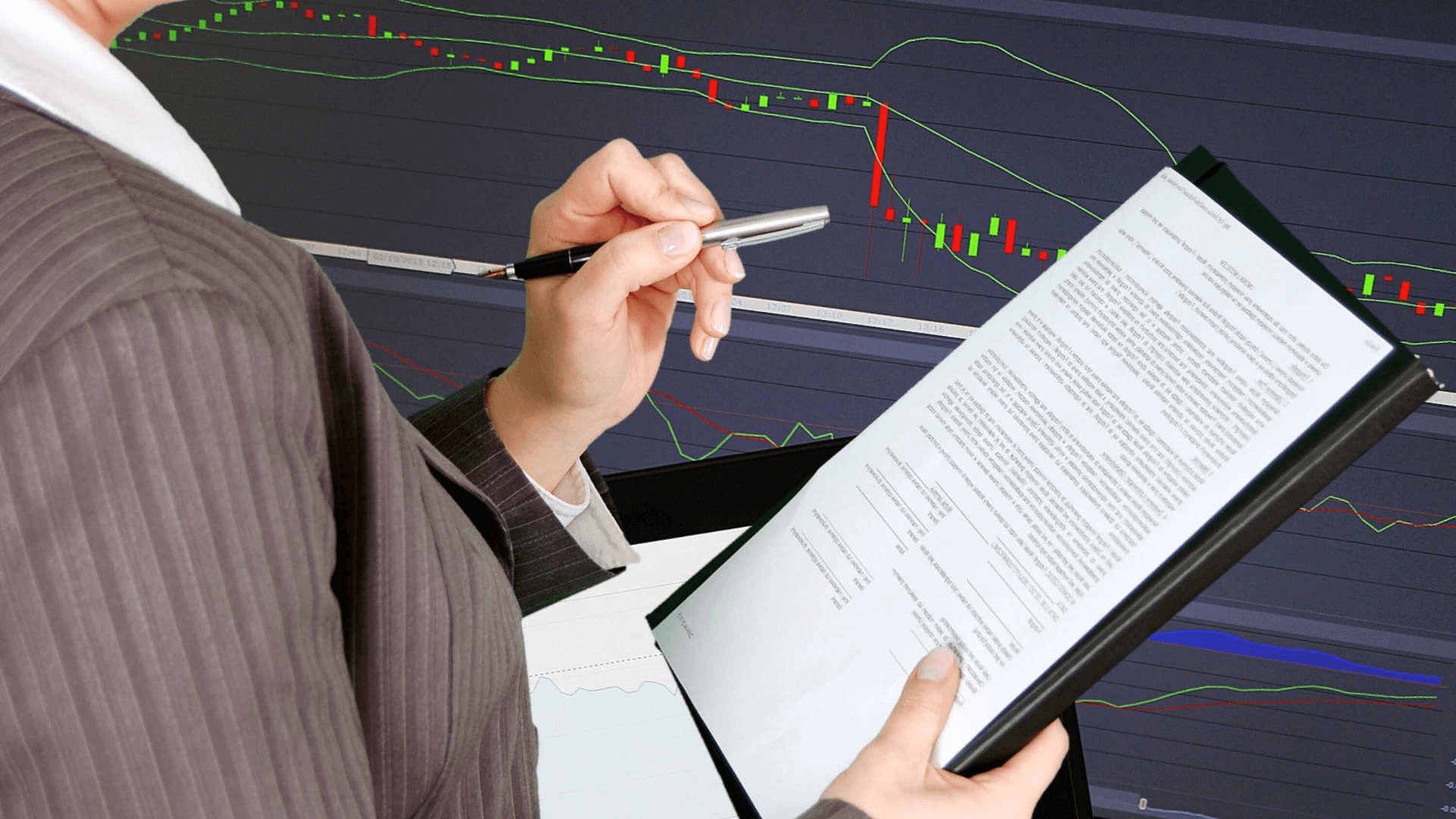 Person reviewing documents near stock charts - Best Prop Firms in Uganda