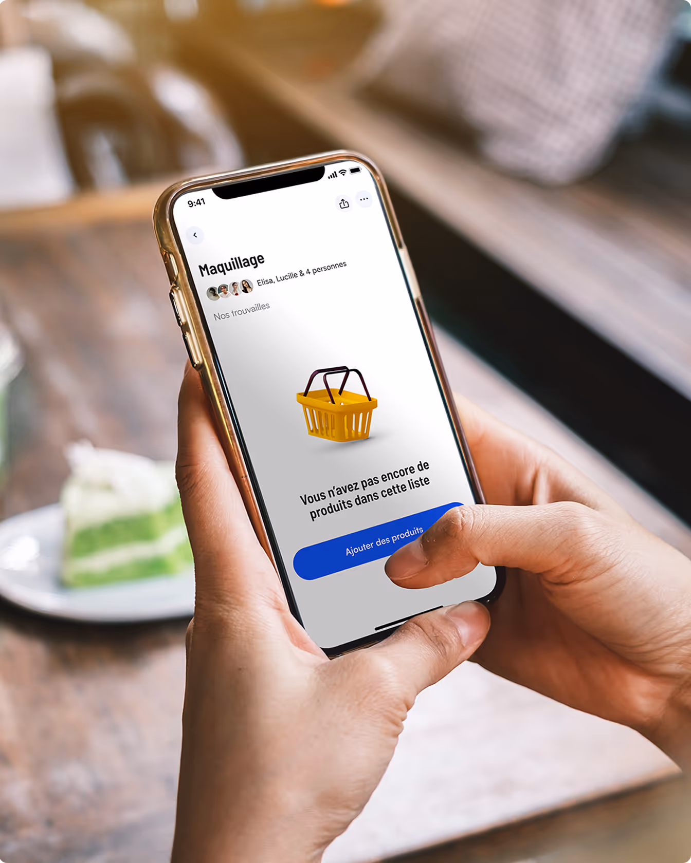 Main tenant un smartphone affichant l’application Quelproduit avec une liste maquillage vide et une illustration de panier jaune sur fond blanc.