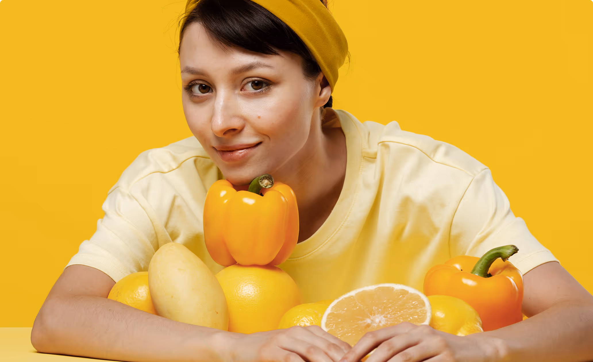 Femme en jaune avec poivron, citron et pamplemousse sur fond jaune.