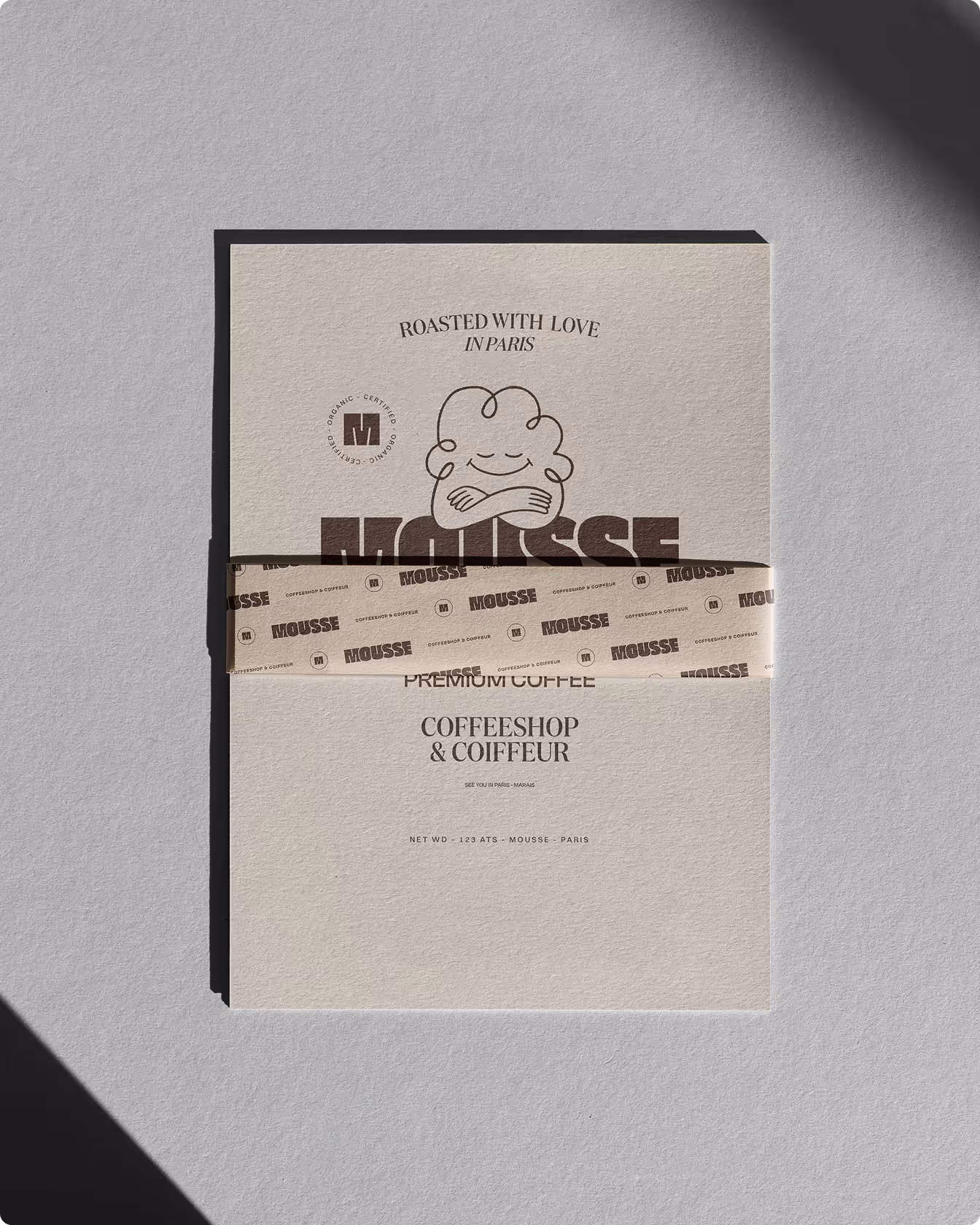 Une étiquette en papier beige Mousse est présentée avec une bande imprimée et éclairée par une lumière naturelle.