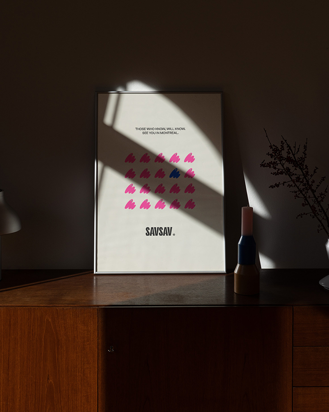 Une affiche encadrée SavSav posée sur un meuble en bois met en avant un design graphique minimaliste.