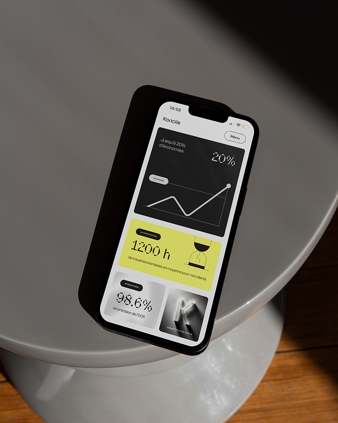 Smartphone posé sur une table affichant interface Koncile avec graphique et solde.