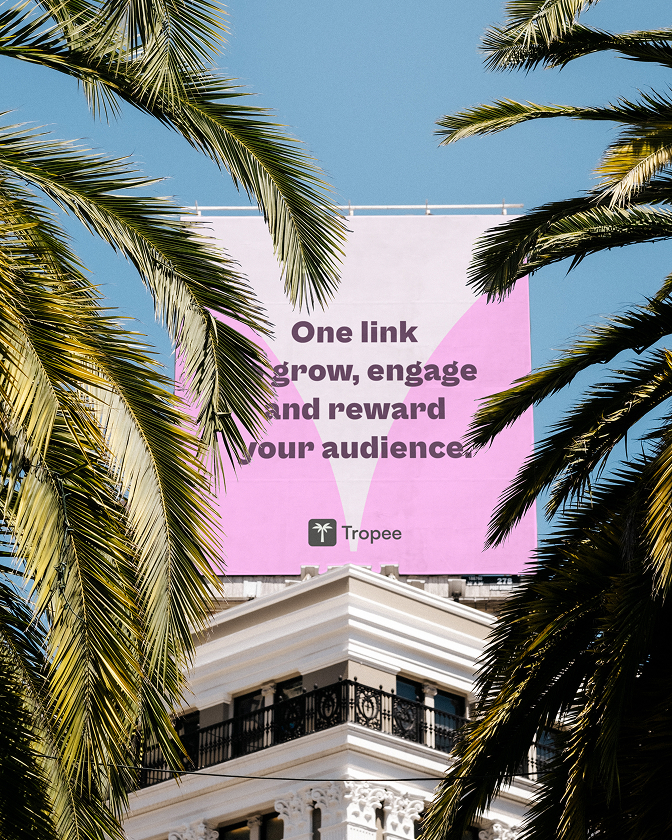 Affiche Tropee sur immeuble à travers des palmiers avec slogan One link grow, engage and reward your audience