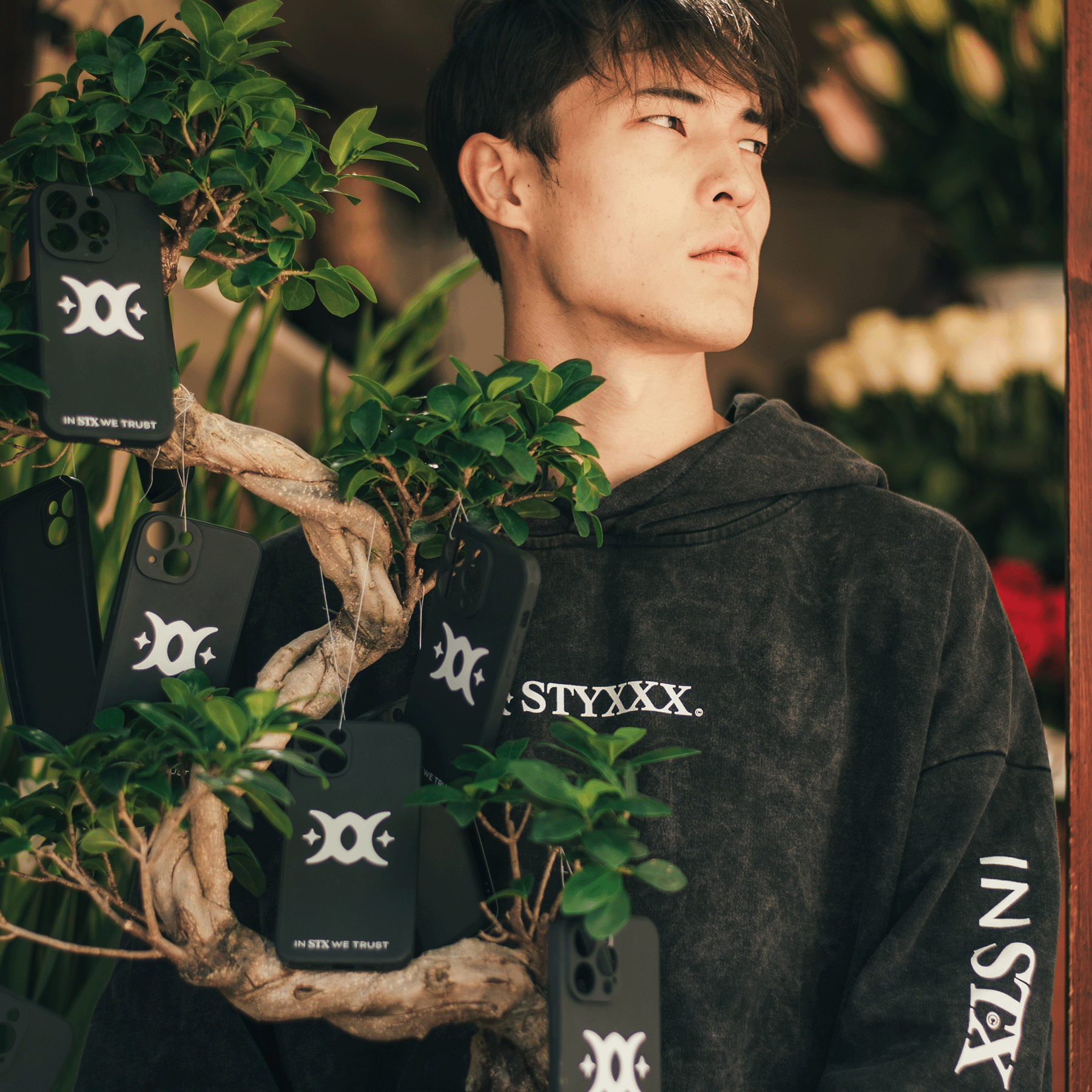 man holding a bonsai tree with iphone cases hanging from the branches 