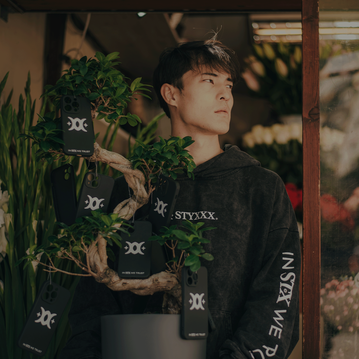 man holding a bonsai tree with iphone cases hanging from the branches 