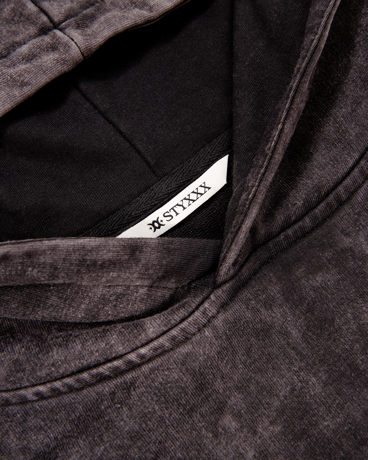 Close-up of a dark gray hooded sweatshirt with a white STYXXX brand label inside the collar.
