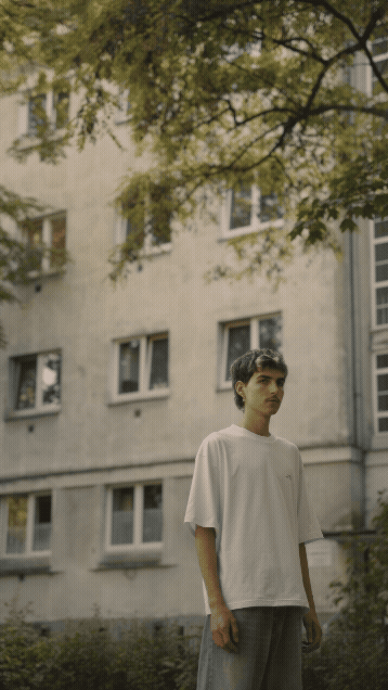 Three young men sitting and standing on a blue playground merry-go-round in an urban outdoor area with a building in the background.