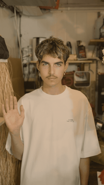 Three young men sitting and standing on a blue playground merry-go-round in an urban outdoor area with a building in the background.