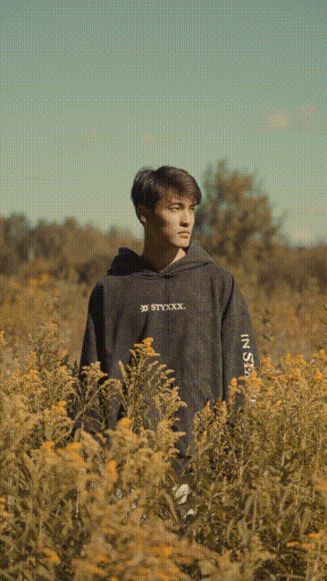 Three young men sitting and standing on a blue playground merry-go-round in an urban outdoor area with a building in the background.