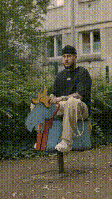 Three young men sitting and standing on a blue playground merry-go-round in an urban outdoor area with a building in the background.