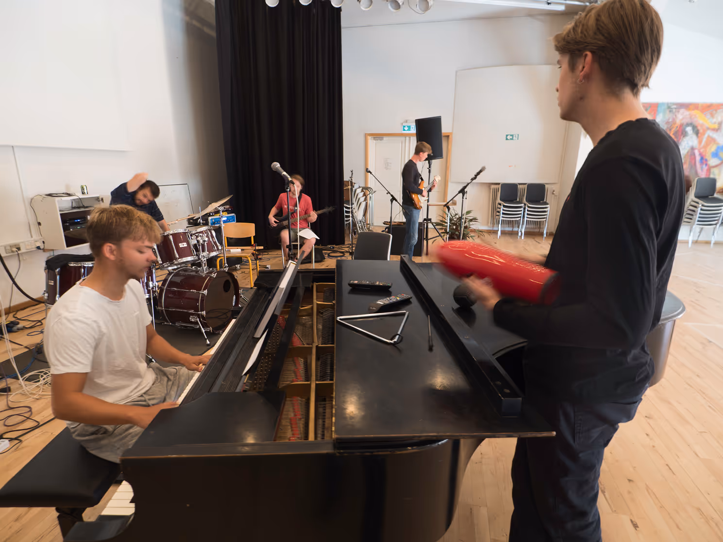 Unge musikere øver sammen med klaver, trommer, bas og guitar i et rummeligt lokale.