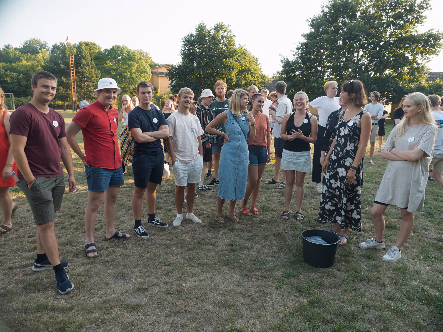 Gruppe af unge mennesker, der står og taler sammen udenfor på en græsplæne på en solrig dag.