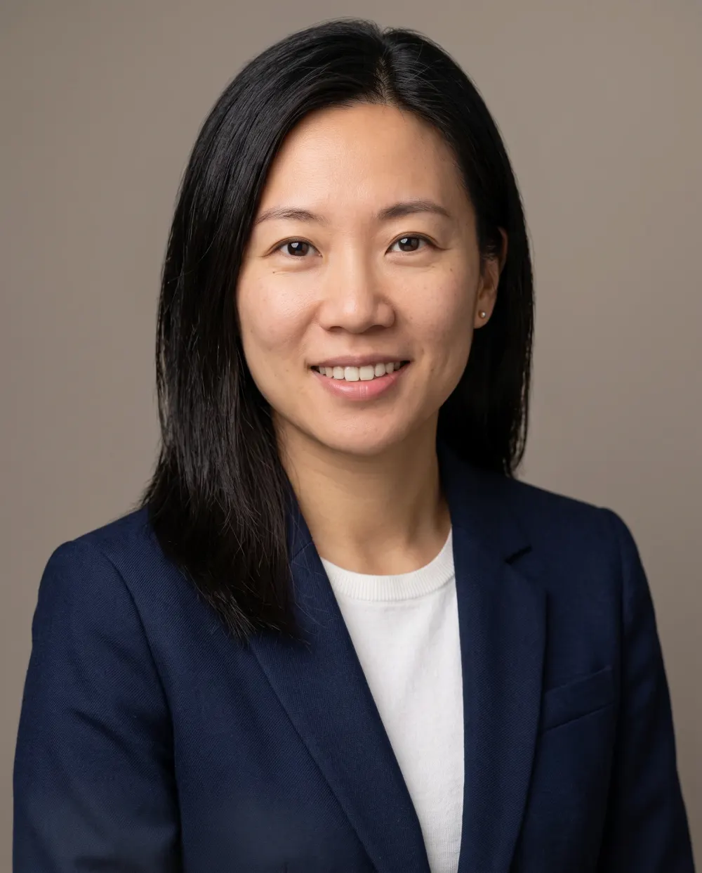 Corporate headshot from a Gemini photo prompt: woman in a navy blazer on warm grey