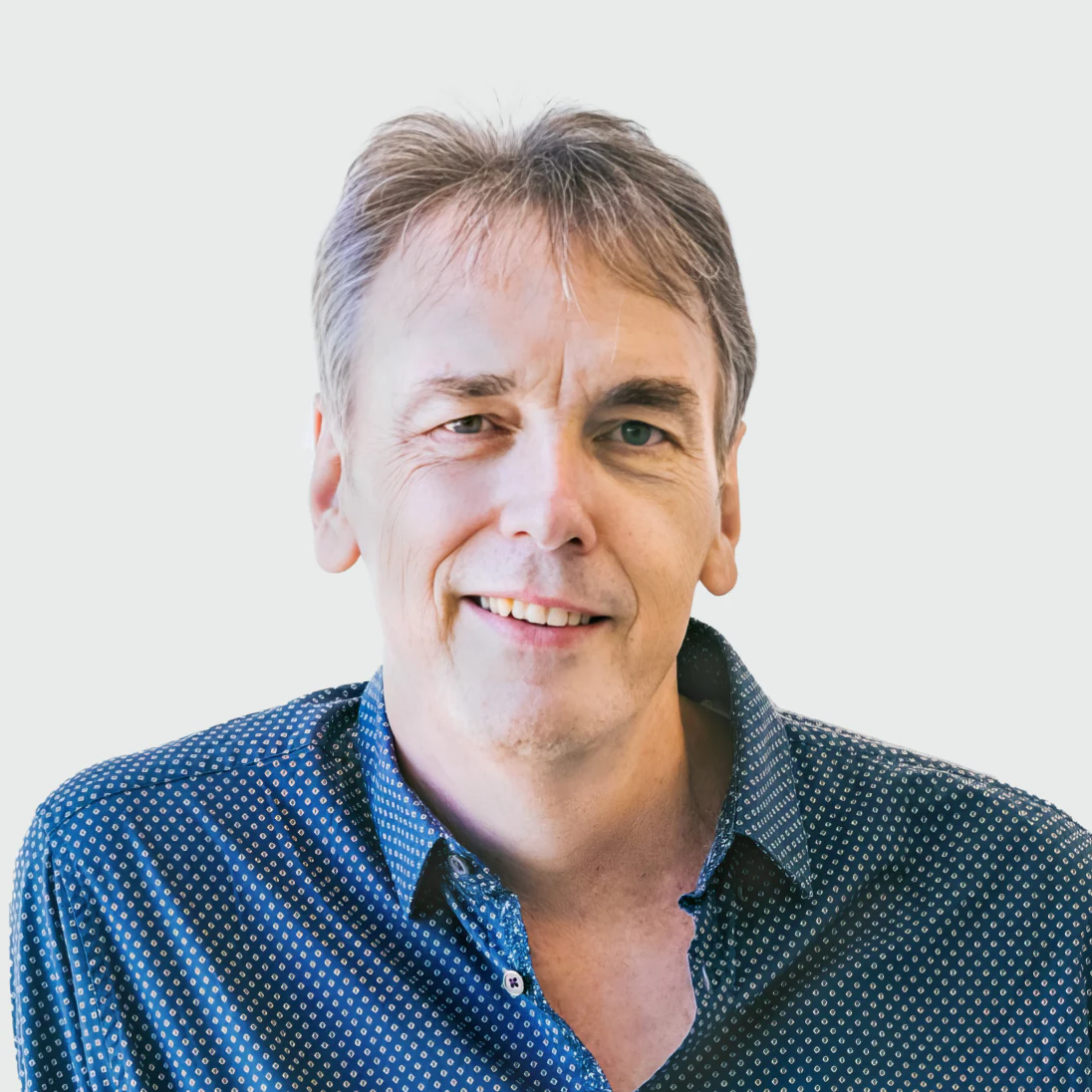 Photo of Professor Sir Peter Donnelly FRS, FMedSci, Founder & CEO of Genomics Ltd, smiling in a checkered shirt.