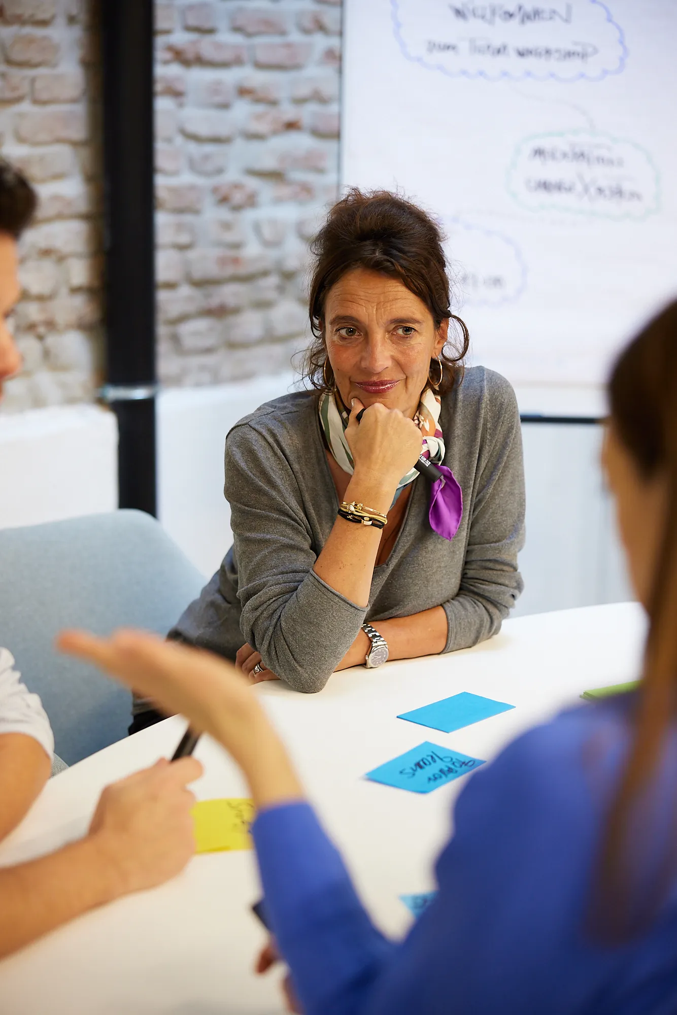 Workshopleiterin hört konzentriert zu, während Teilnehmerin spricht – Flipchart im Hintergrund