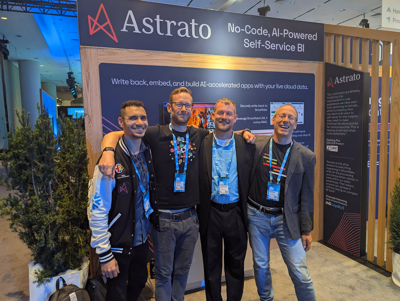 Four men standing with arms around each other smiling in front of an Astrato AI-powered self-service BI booth.