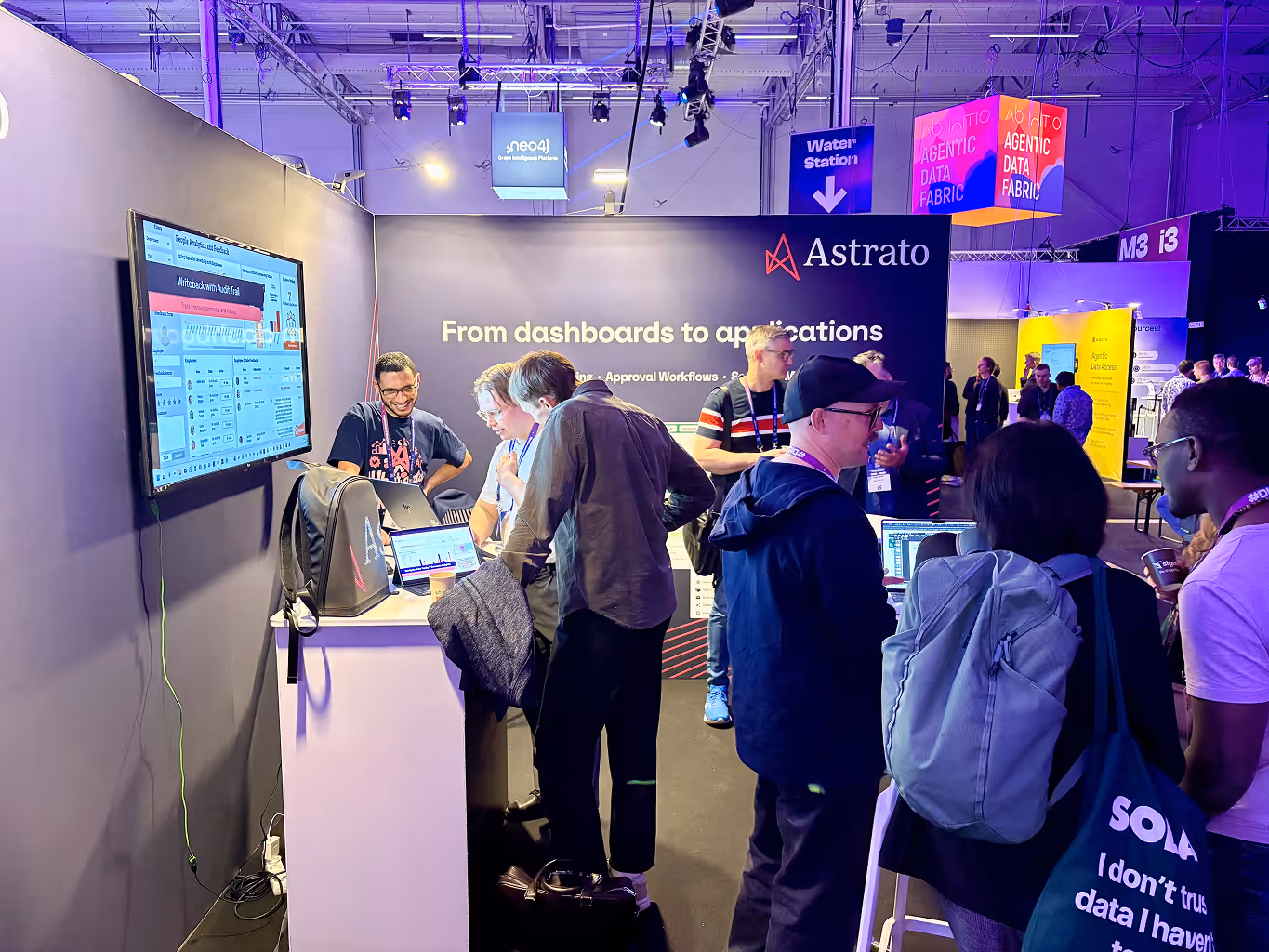 People engaging at Astrato booth with laptops and a display showing dashboard analytics at a tech event.
