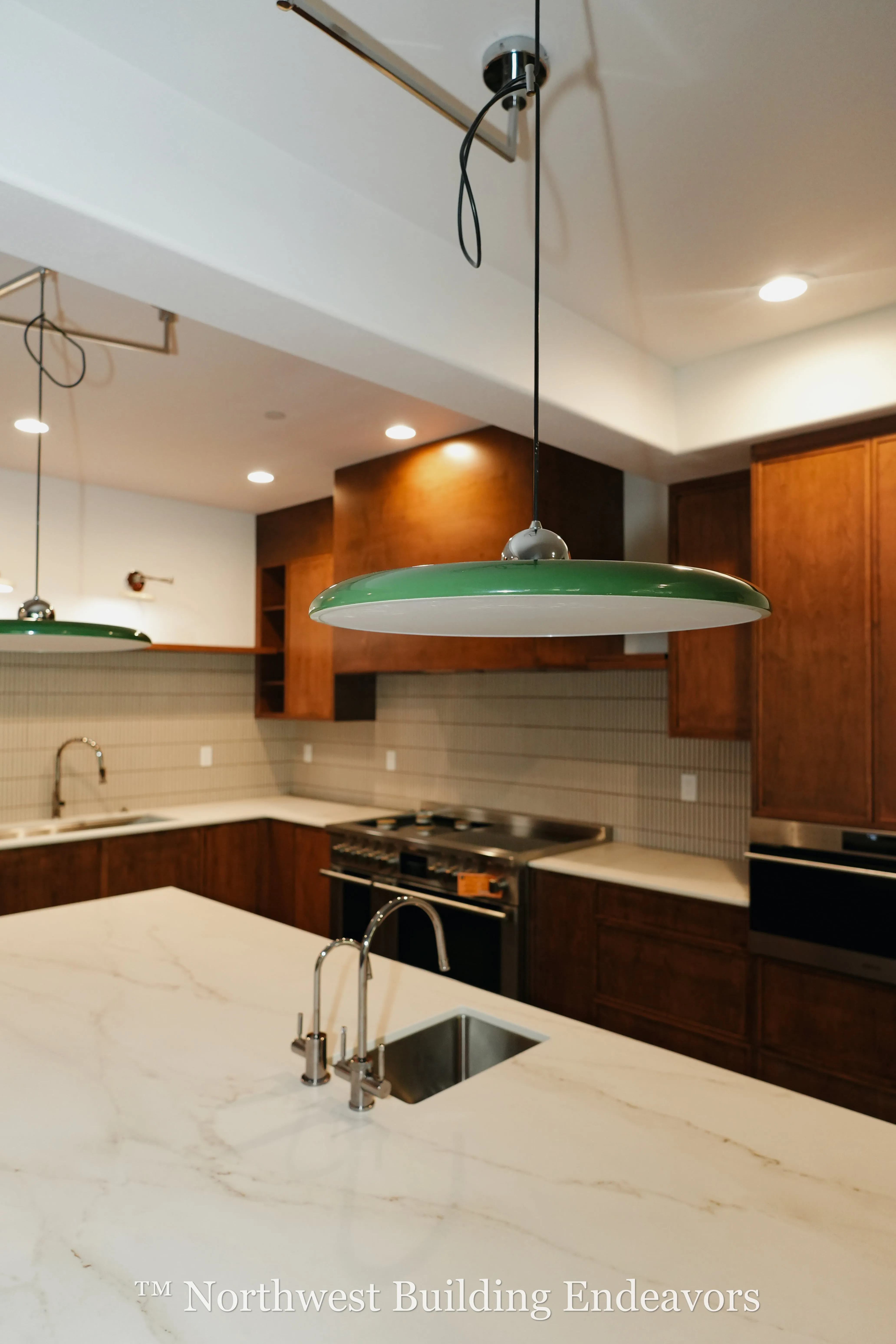 Modern kitchen with marble countertop island, stainless steel sink, green pendant lights, and wooden cabinets.