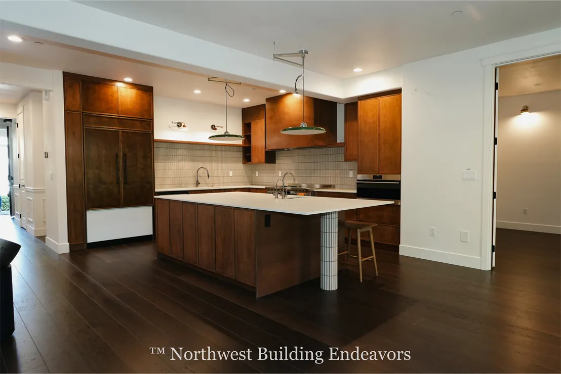 Modern kitchen with dark wood cabinetry, a large white island with built-in sink, pendant lights, and dark hardwood floors.