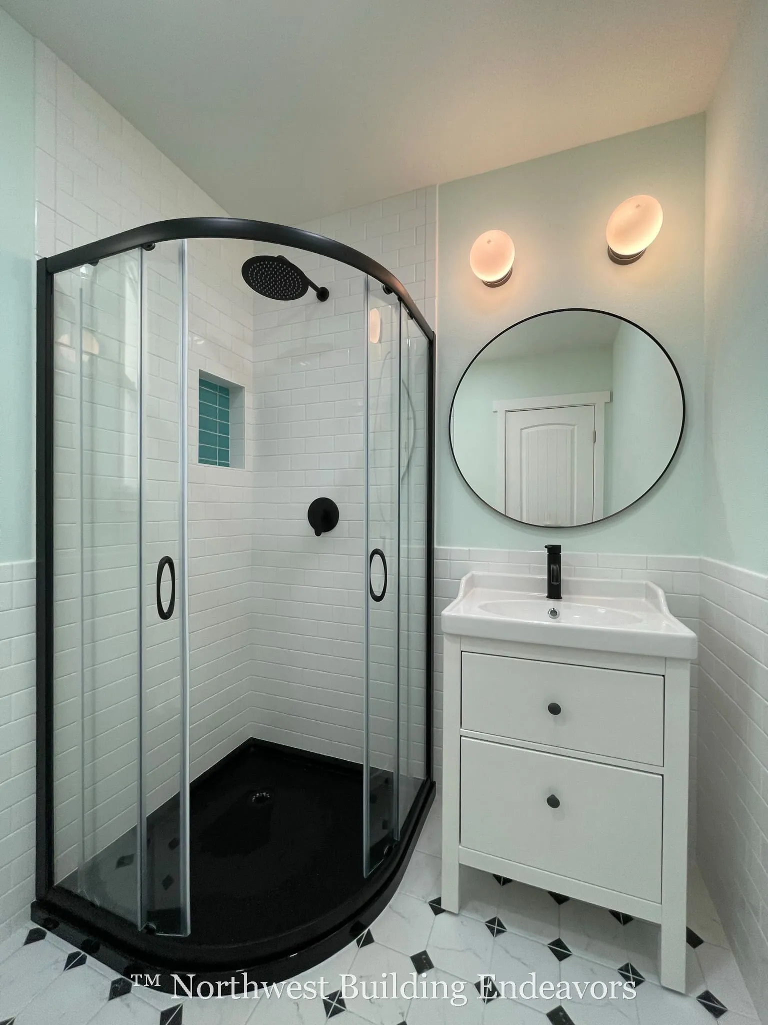 Modern bathroom with a glass-enclosed corner shower featuring black fixtures and a white vanity with a round mirror and two wall lights above.