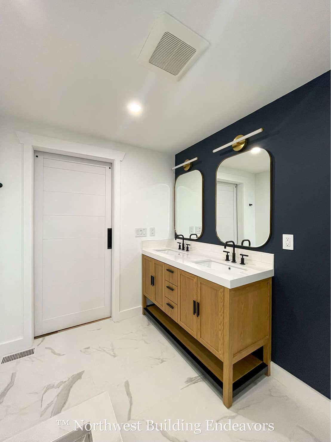 A small wooden guest house with large glass sliding doors and warm interior lighting, next to a larger house during twilight.