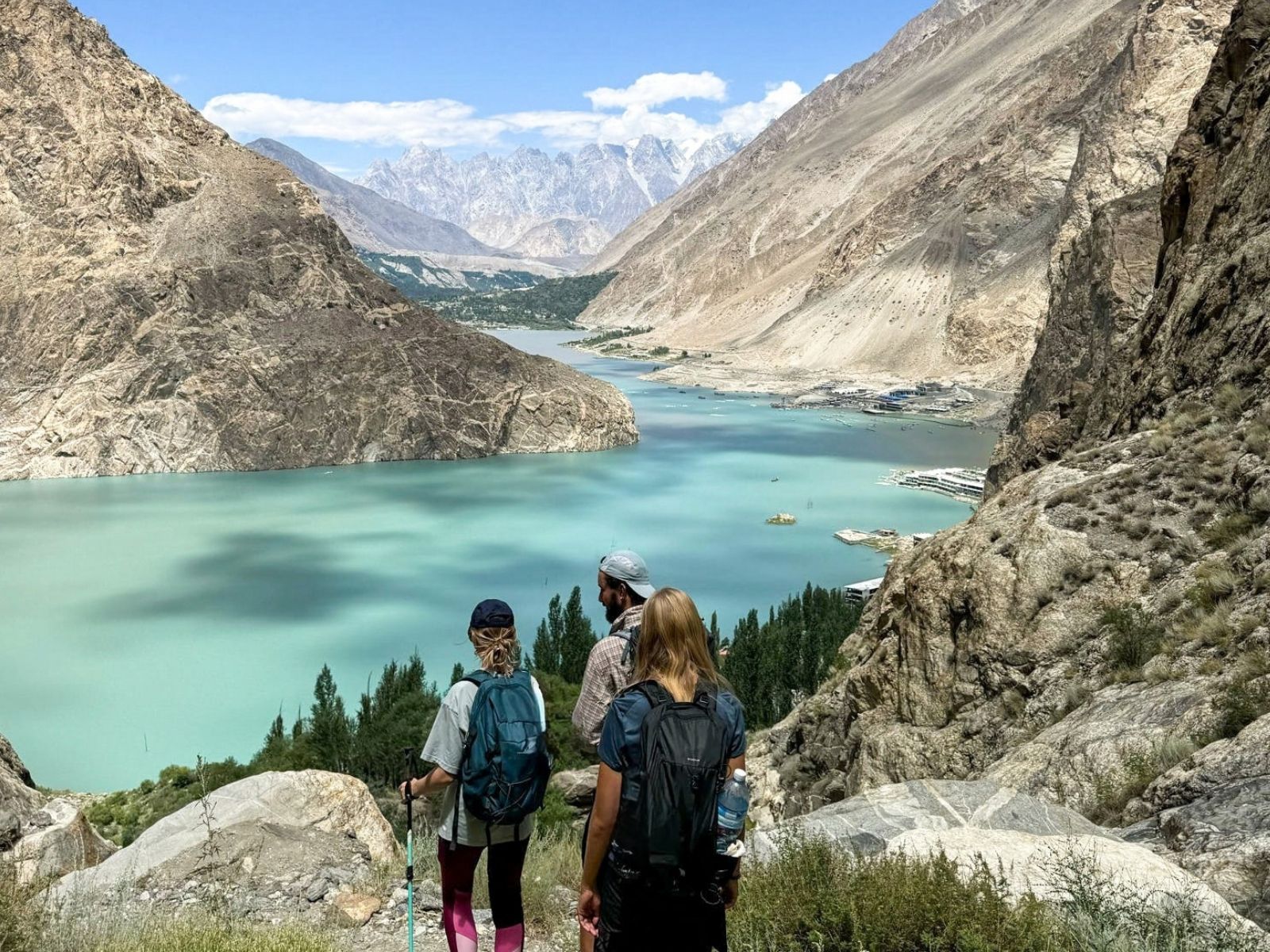 Hikers looking over the turquoise water of Attabad Lake from Baskochi Meadows, Pakistan