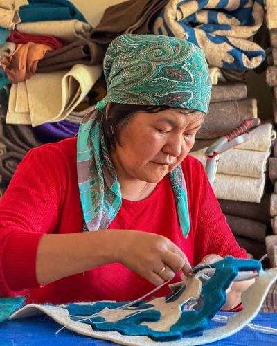 Kyrgyz woman sewing a felt carpet during a cultural masterclass
