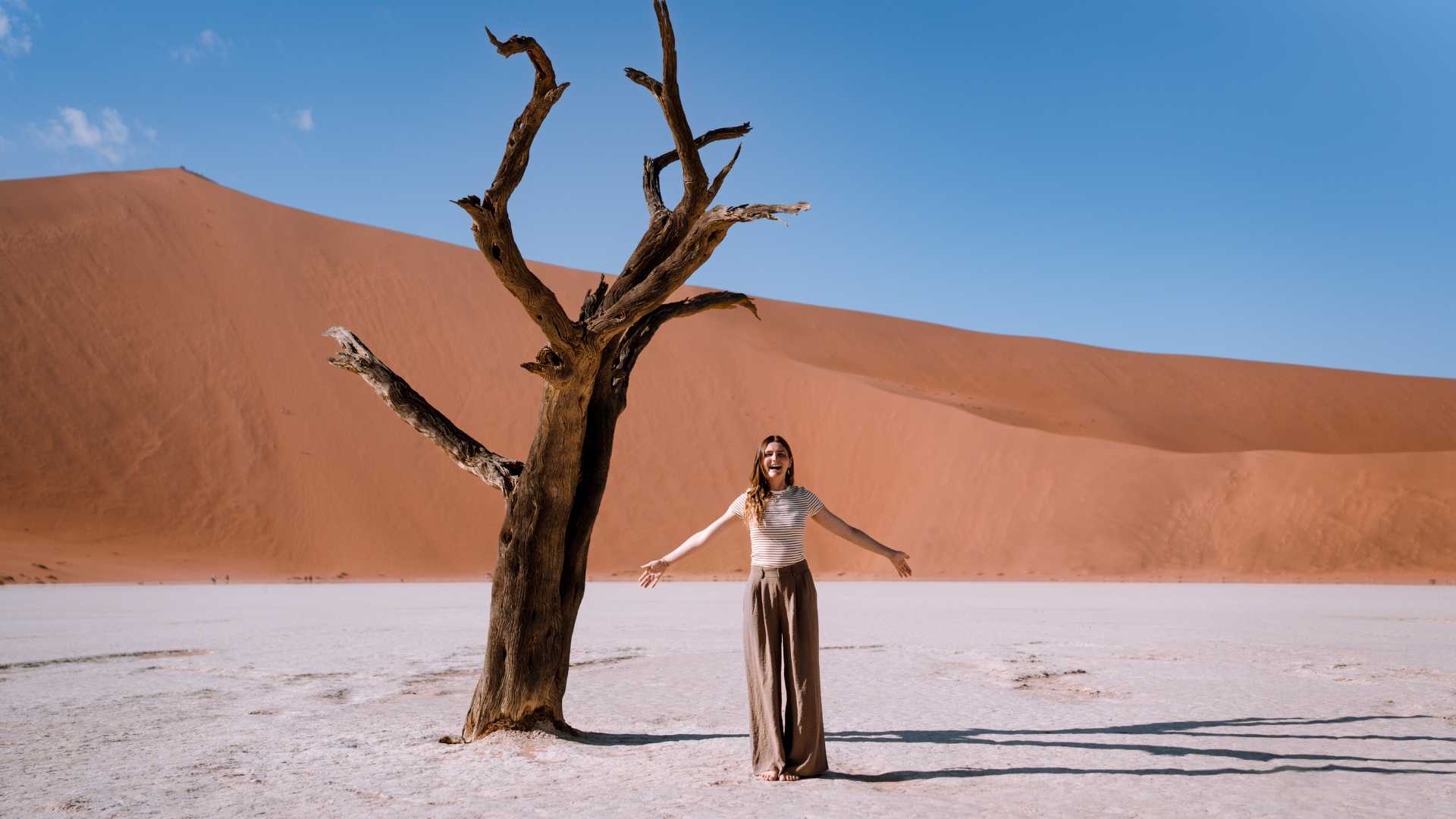 Woman standing beside a dead camel thorn tree in Deadvlei, Namibia