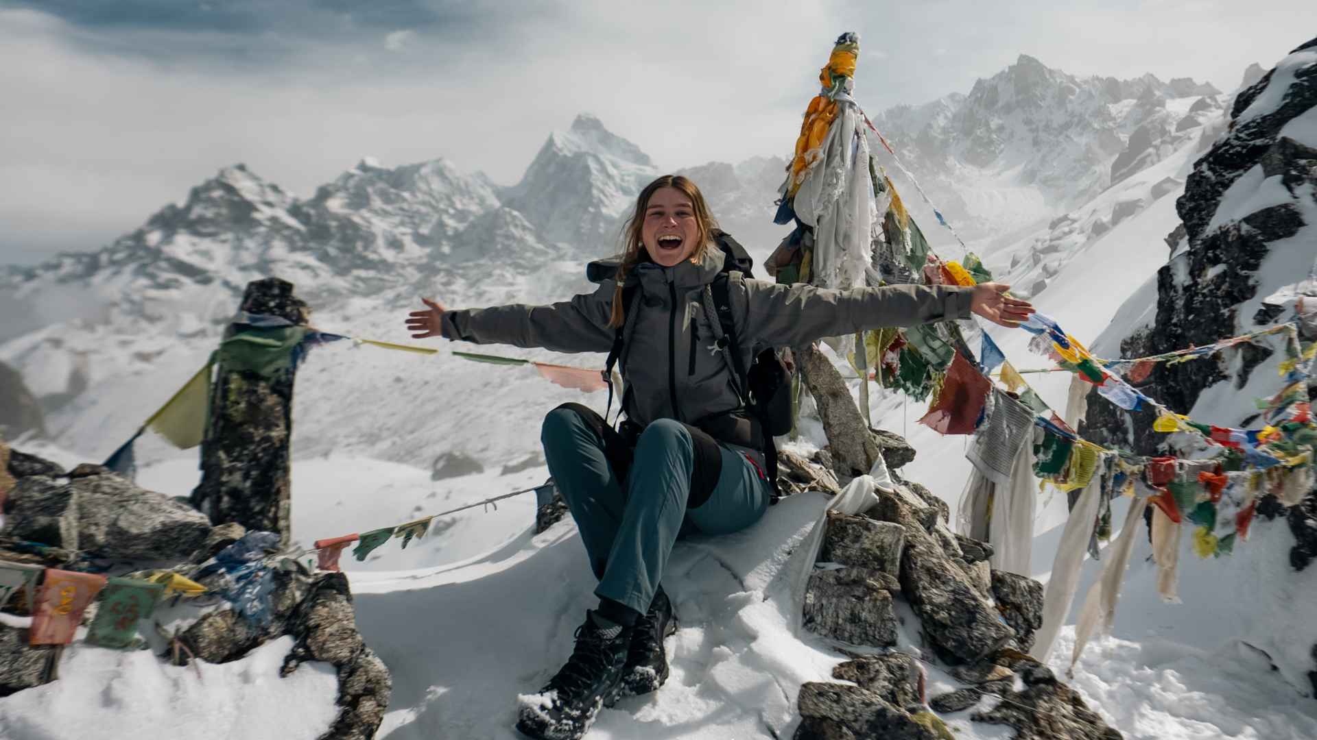 Hiker with arms outstretched beside prayer flags on the Kanchenjunga Circuit, Nepal