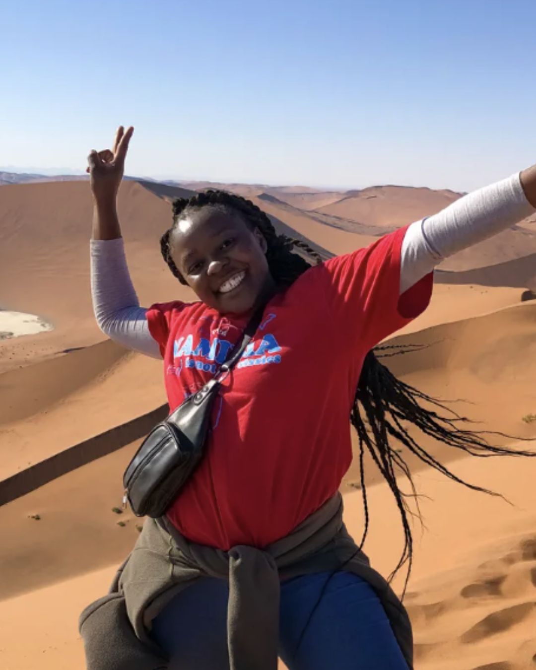 Smiling tour guide with her arms raised on a sand dune in Namibia