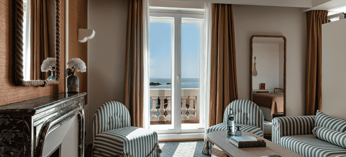 Intérieur lumineux avec canapé et fauteuils à rayures, grandes fenêtres et panorama océan en arrière-plan