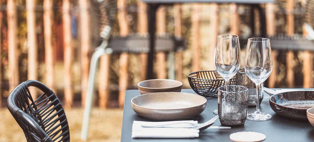 Table dressée en terrasse au restaurant Le Garage à Biarritz, chaises en rotin noir autour d'une table avec verres et assiettes.