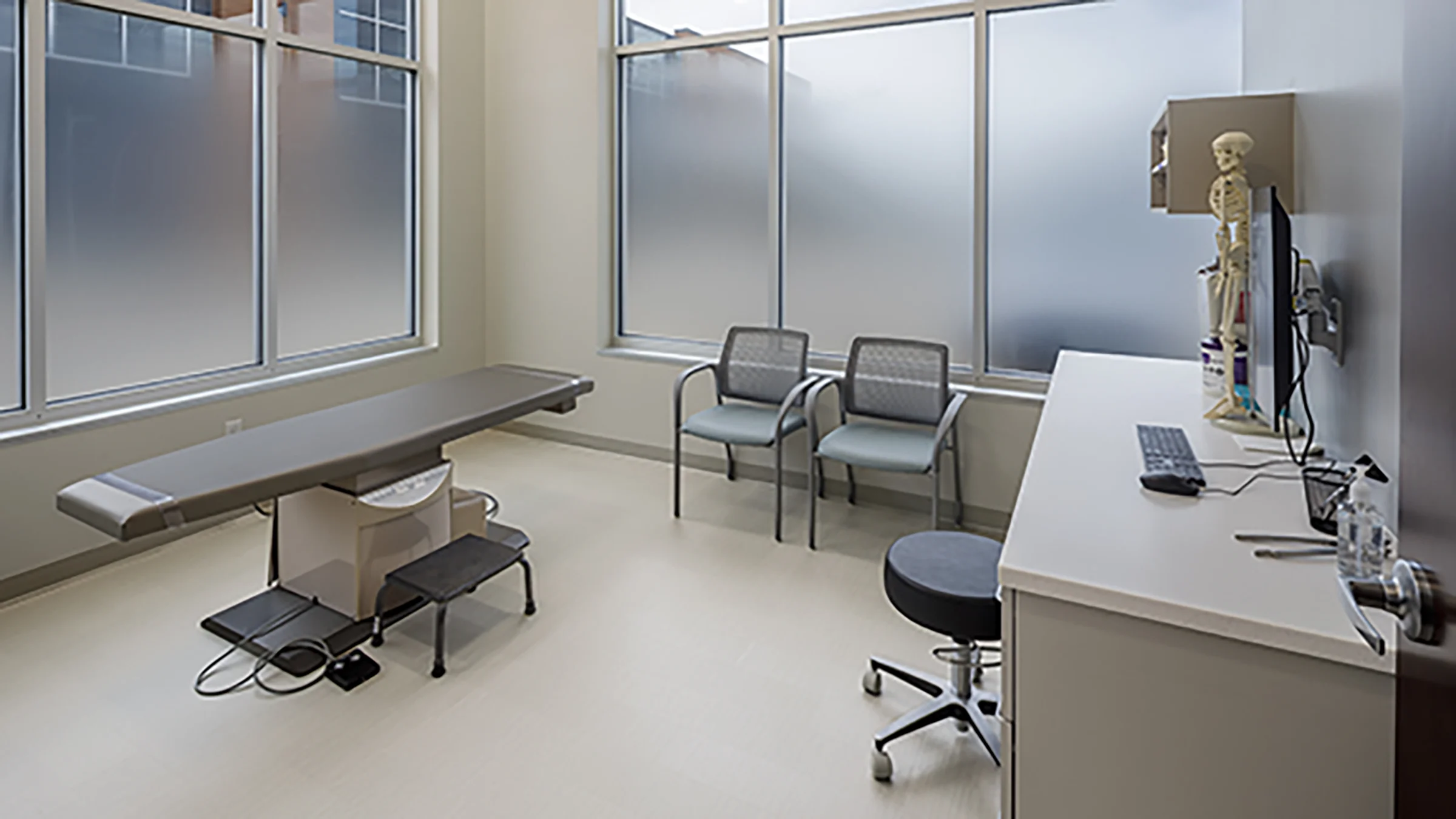 Physical therapy examination room with table, chairs and desk.