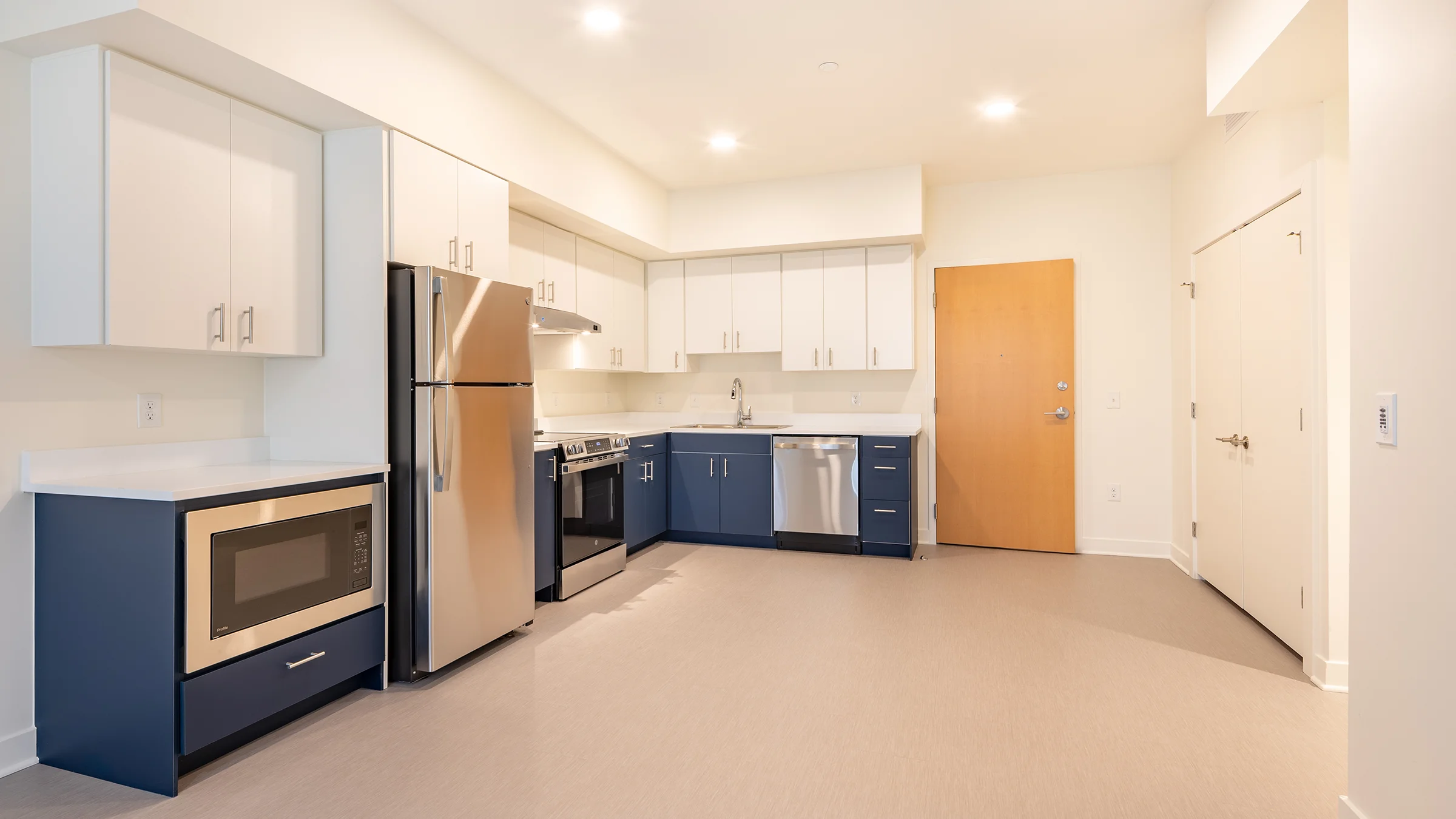 Large kitchen space in apartment with stainless steel appliances and blue cabinets.