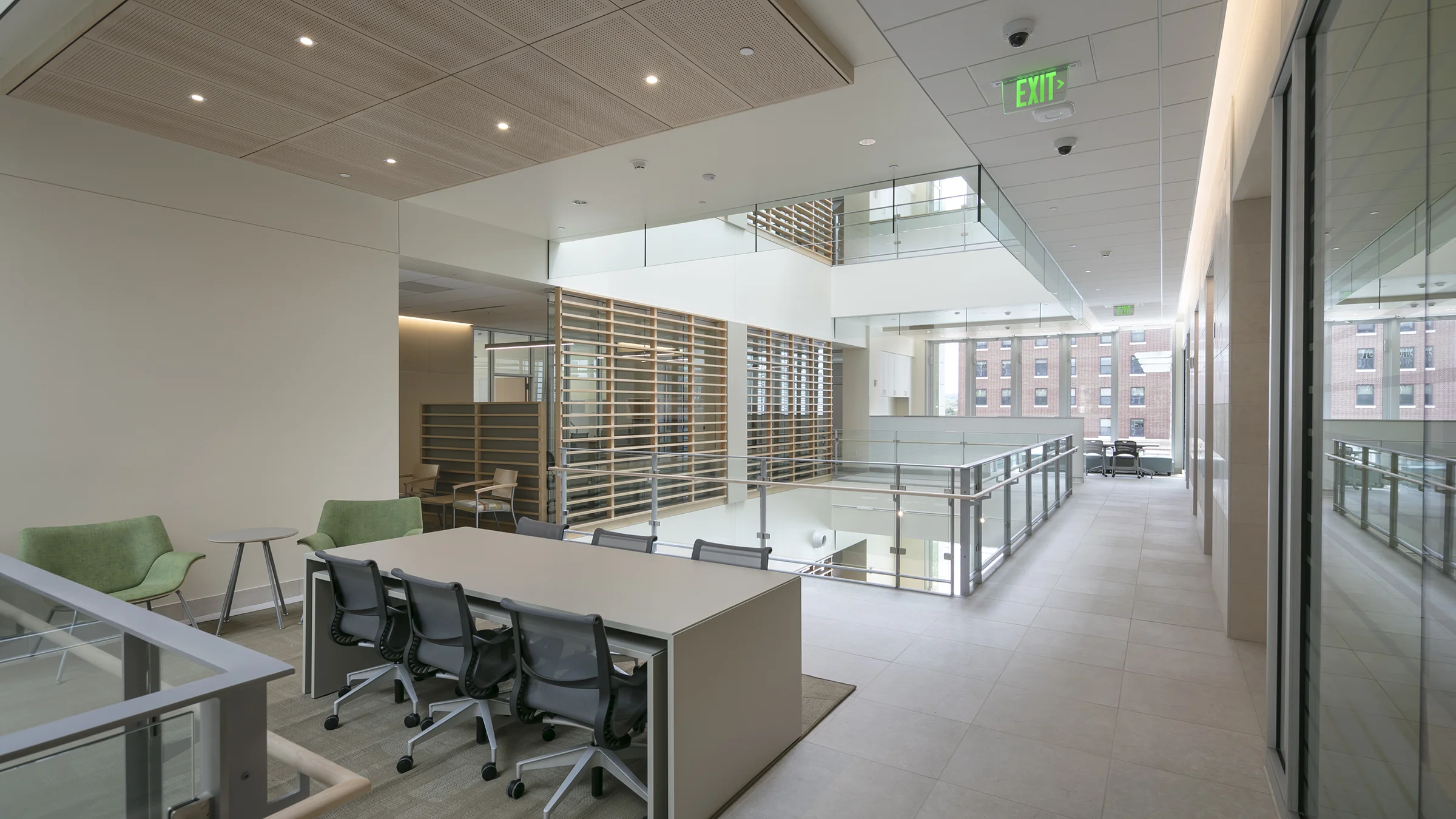 2nd floor work area with table and rolling chairs. The open area is bright with glass railings and wooden privacy screens.