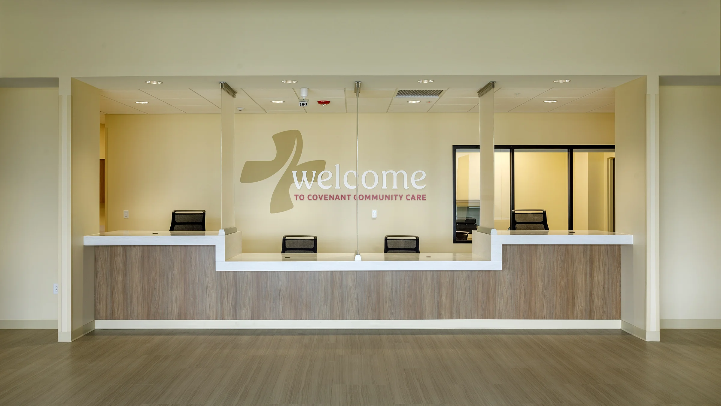 Check-in desk of Covenant Community Care's Joy Road Clinic. The walls are butter yellow and the desk is a warm wood.
